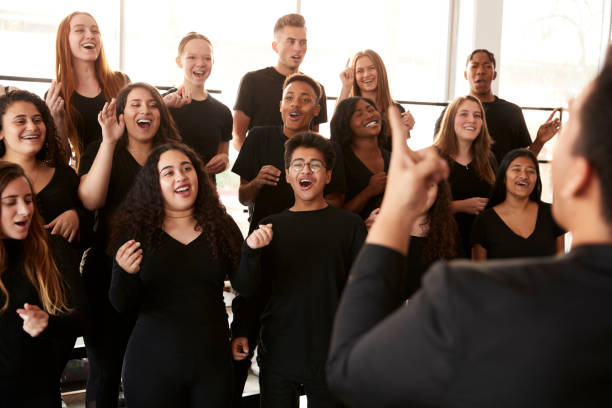 Male And Female Students Singing In Choir With Teacher At Performing Arts School